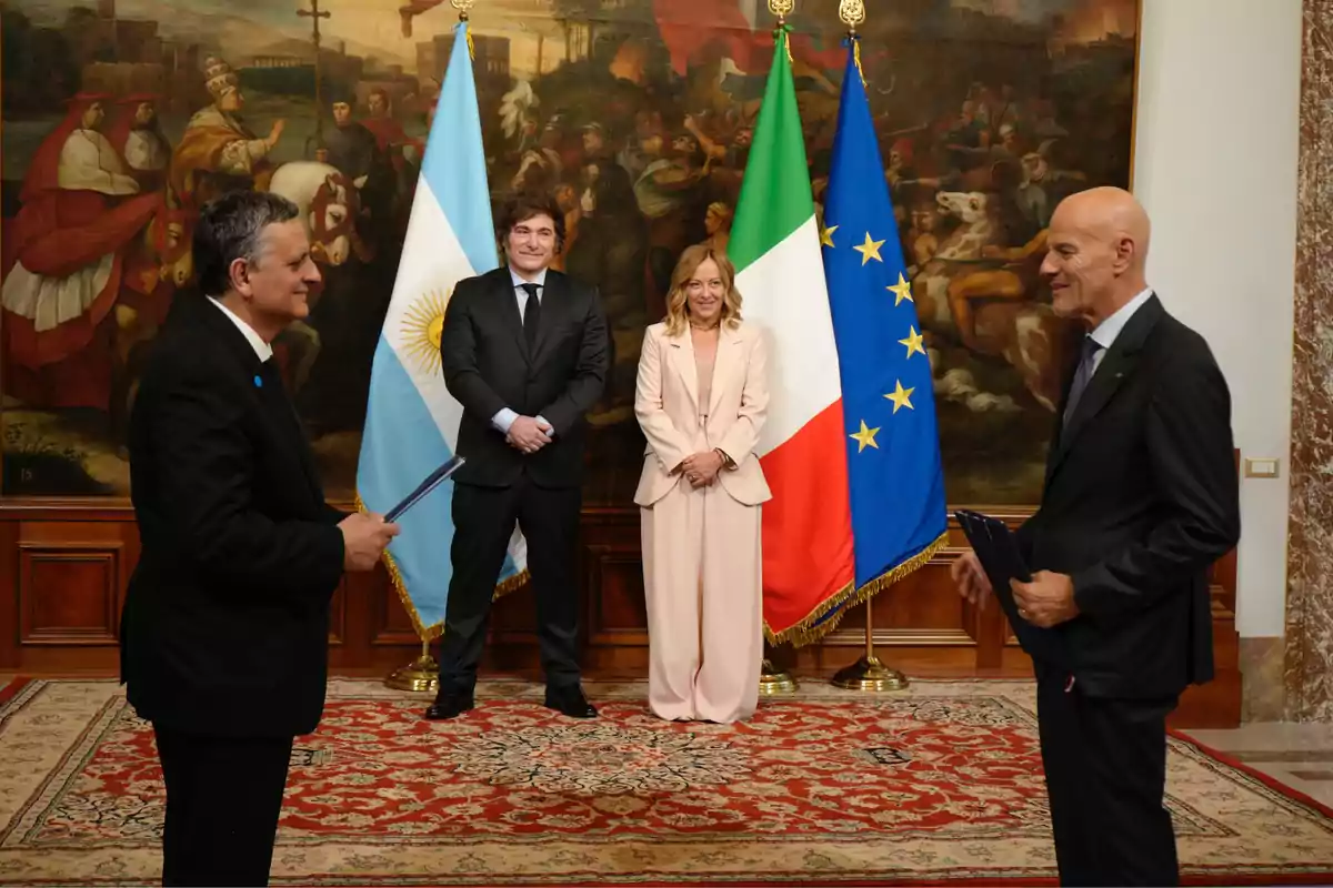 Cuatro personas vestidas de traje posan en una sala elegante con alfombra roja y un gran cuadro al fondo, detrás de ellos hay banderas de Argentina, Italia y la Unión Europea. Cuatro personas vestidas de traje posan en una sala elegante con alfombra roja y un gran cuadro al fondo, detrás de ellos hay banderas de Argentina, Italia y la Unión Europea.