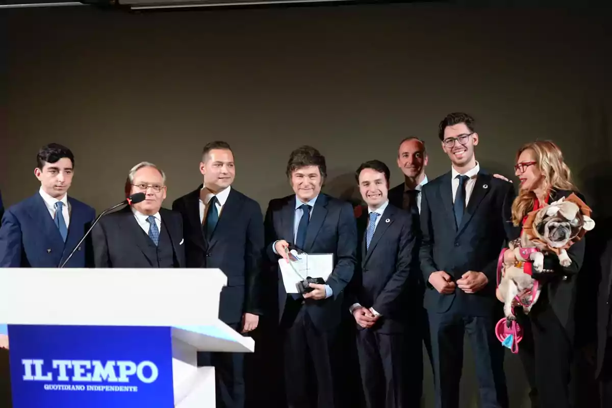 Un grupo de personas vestidas formalmente posando en un evento con un podio que tiene el logo de "Il Tempo" y una mujer sosteniendo un perro.