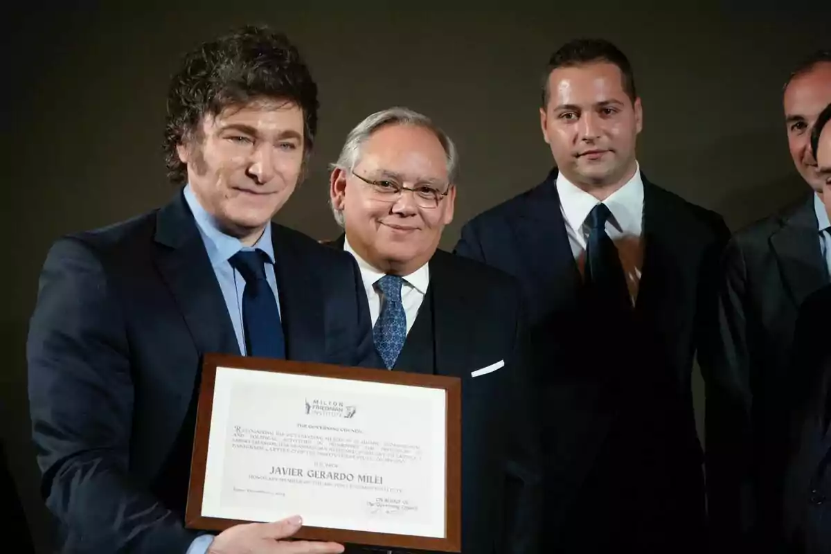 Un grupo de hombres en traje posan para una foto, uno de ellos sostiene un diploma enmarcado.