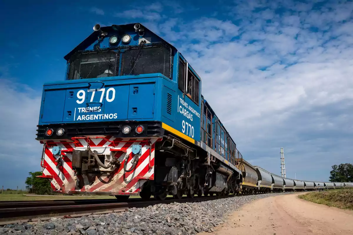 Una locomotora azul de Trenes Argentinos Cargas avanza sobre las vías en un día despejado.