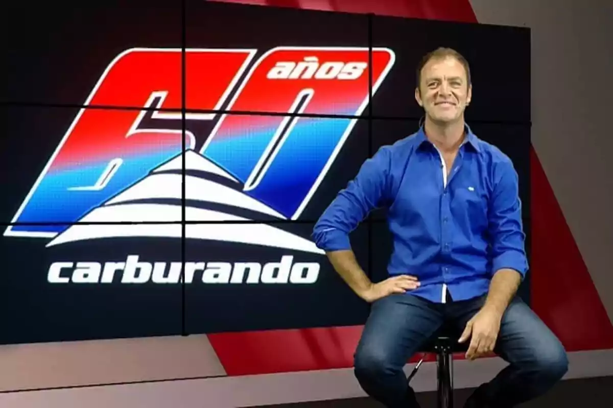 Smiling man in a blue jersey sitting on a bench in front of a screen displaying the 60 Years Carburando logo