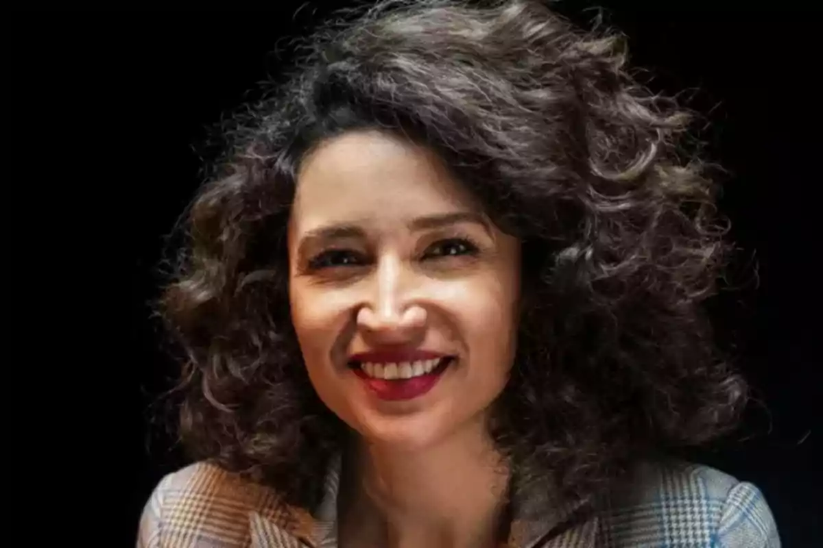 Una persona con cabello rizado y sonrisa amplia en un fondo oscuro.