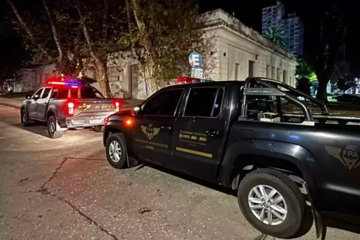 Dos camionetas de la policía están estacionadas en una calle por la noche con las luces encendidas frente a un edificio antiguo