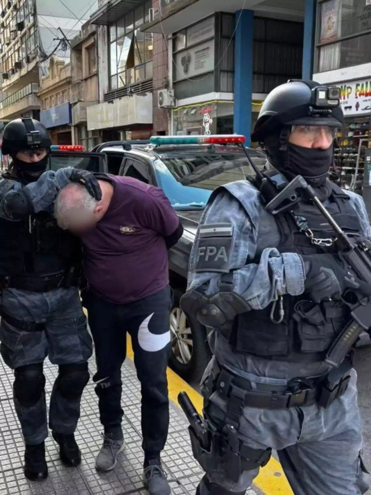 Policías fuertemente armados detienen a un hombre en la vía pública frente a un edificio comercial Policías fuertemente armados detienen a un hombre en la vía pública frente a un edificio comercial