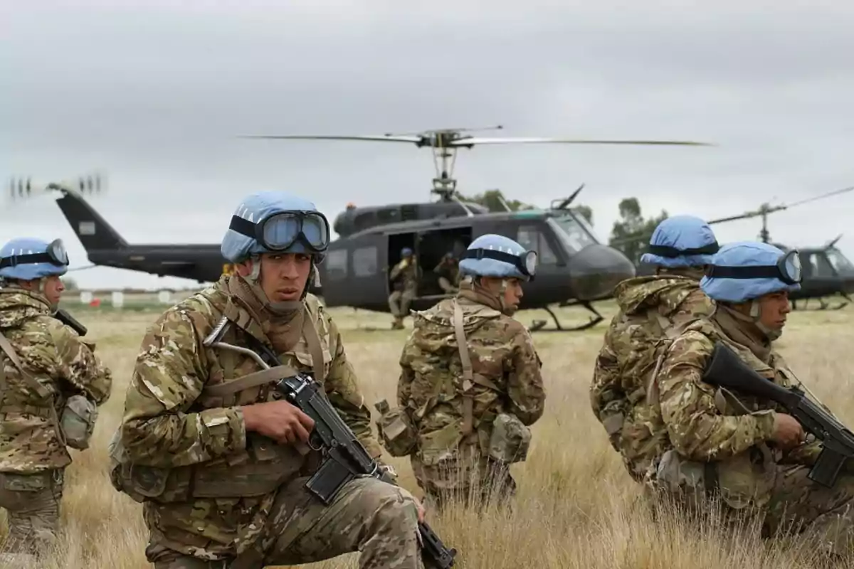 Soldados con cascos azules y uniformes de camuflaje se preparan junto a helicópteros militares en un campo abierto.