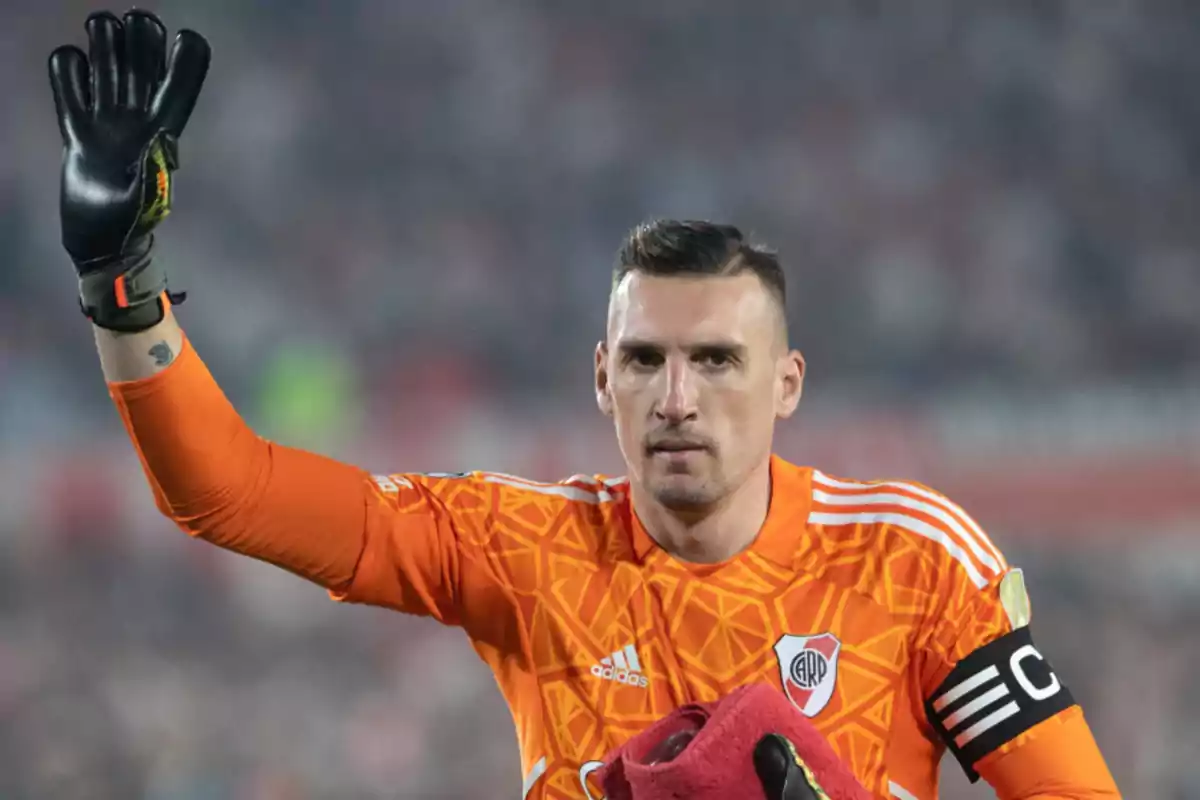 Un futbolista con uniforme naranja levanta la mano en un estadio.