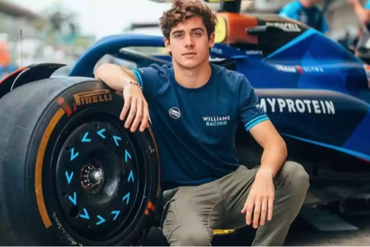 Persona sentada junto a un auto de carreras con camiseta de Williams Racing.