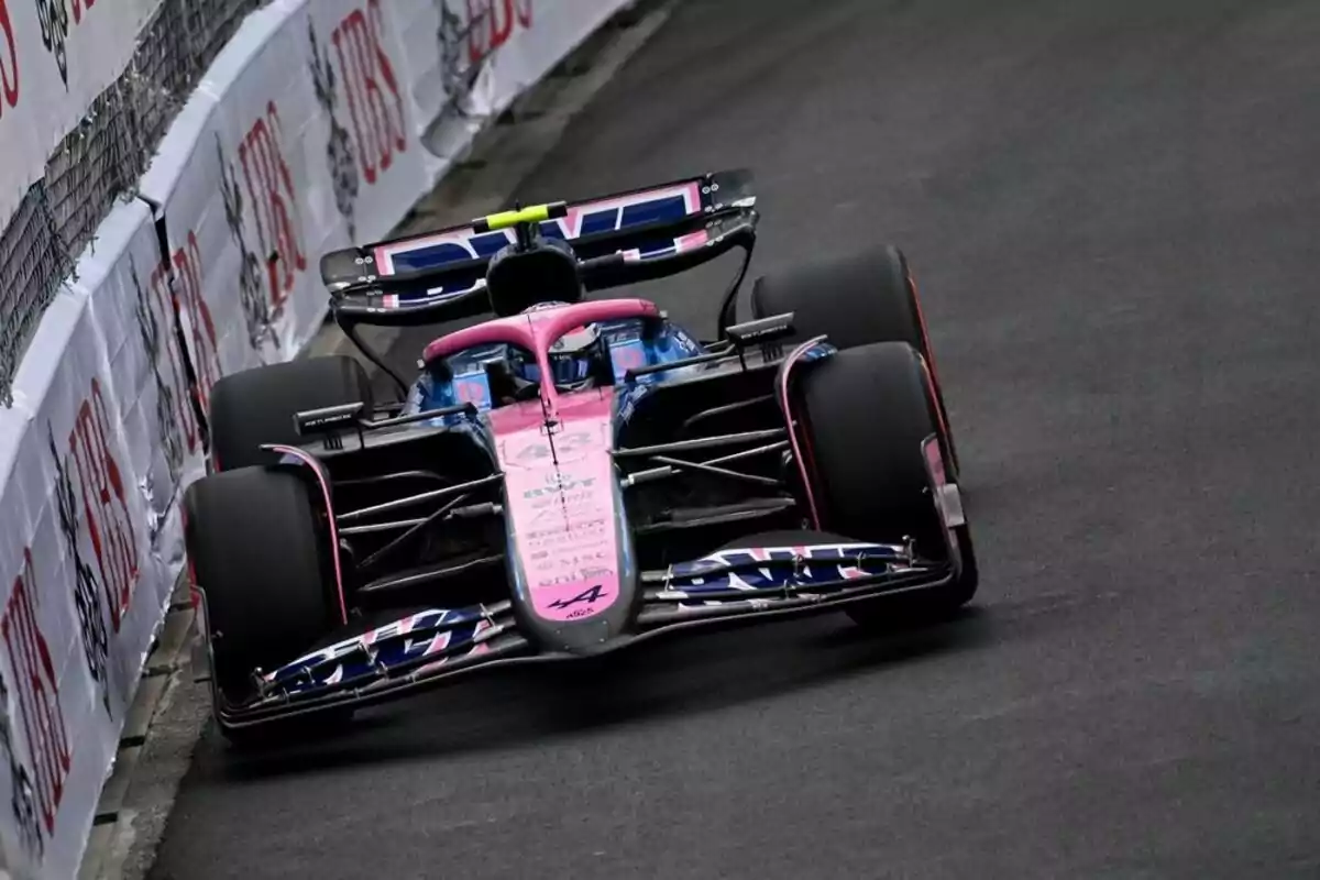 A pink and blue Formula 1 car is driving near the wall on a city race track. A pink and blue Formula 1 car is driving near the wall on a city race track.