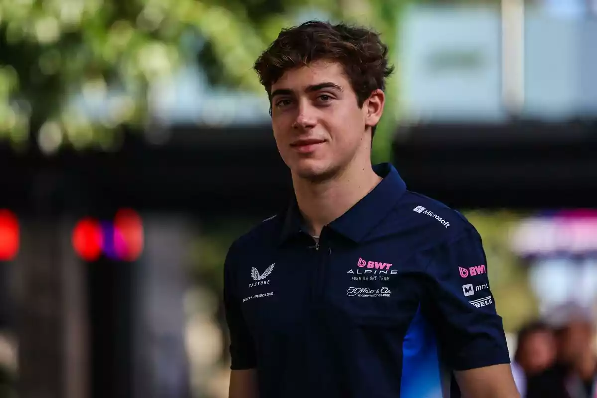 Young man with brown hair and a blue Formula 1 team jersey posing outdoors with a blurred background