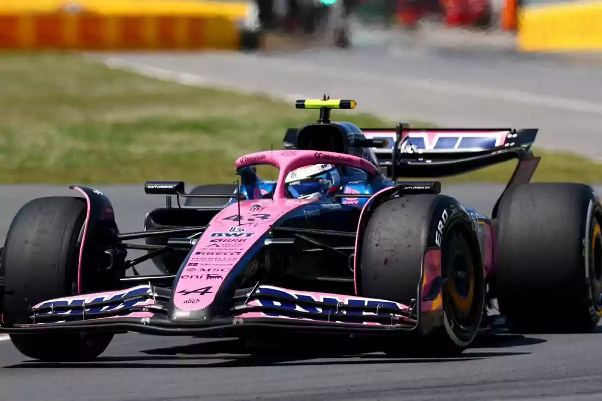Un auto de Fórmula 1 color rosa y azul circula por una pista de carreras durante una competencia Un auto de Fórmula 1 color rosa y azul circula por una pista de carreras durante una competencia