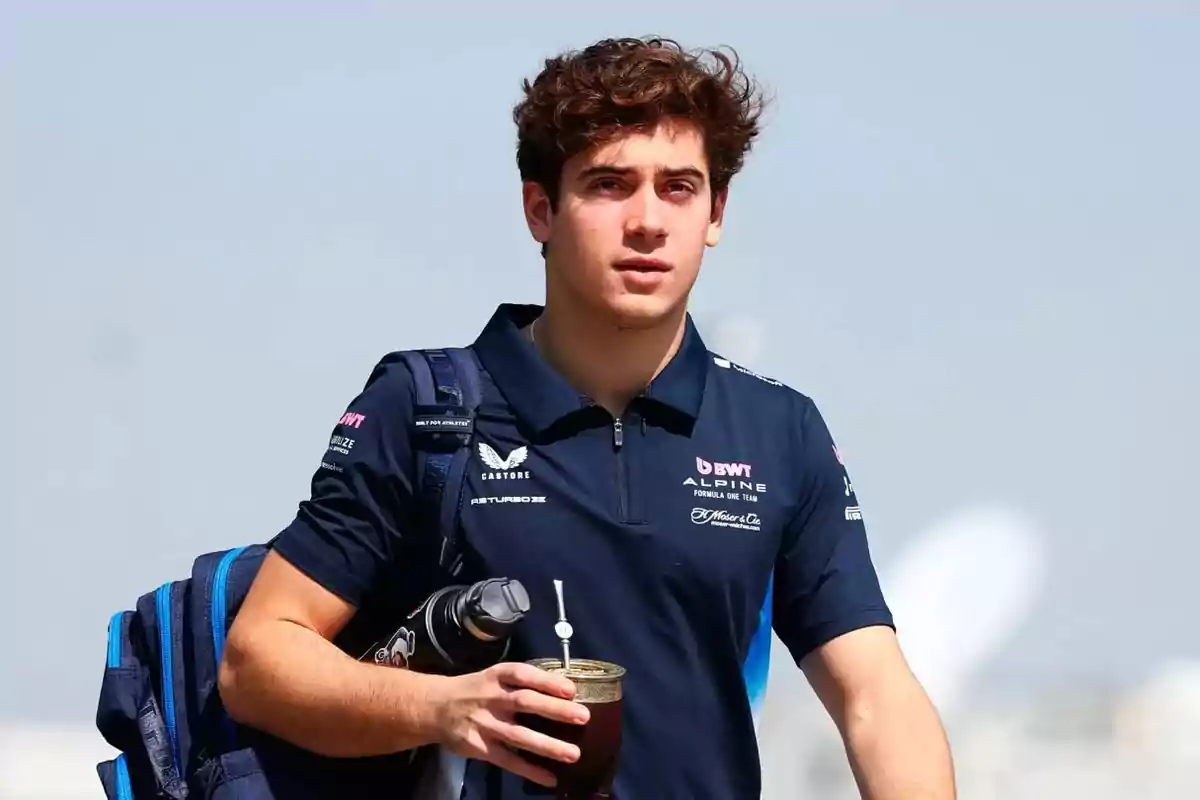Un joven con camiseta azul y mochila lleva un termo y un mate en la mano.
