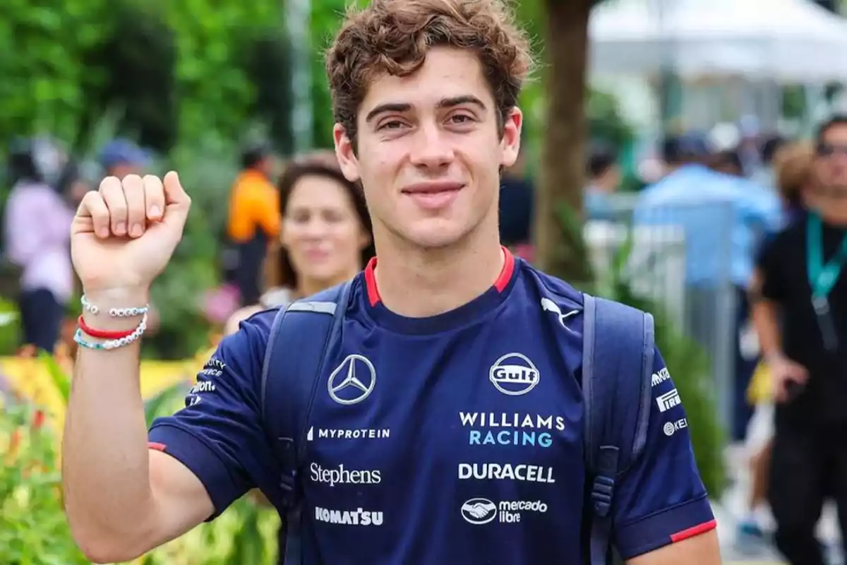 Joven con camiseta de Williams Racing levantando el puño en un entorno al aire libre.