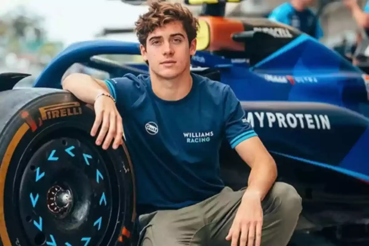 Joven con camiseta de Williams Racing posando junto a un auto de carreras.