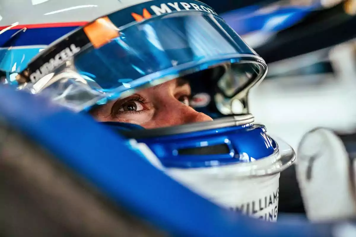 Un piloto de carreras con casco y visera azul se prepara para la competencia, mostrando una mirada concentrada y determinada.