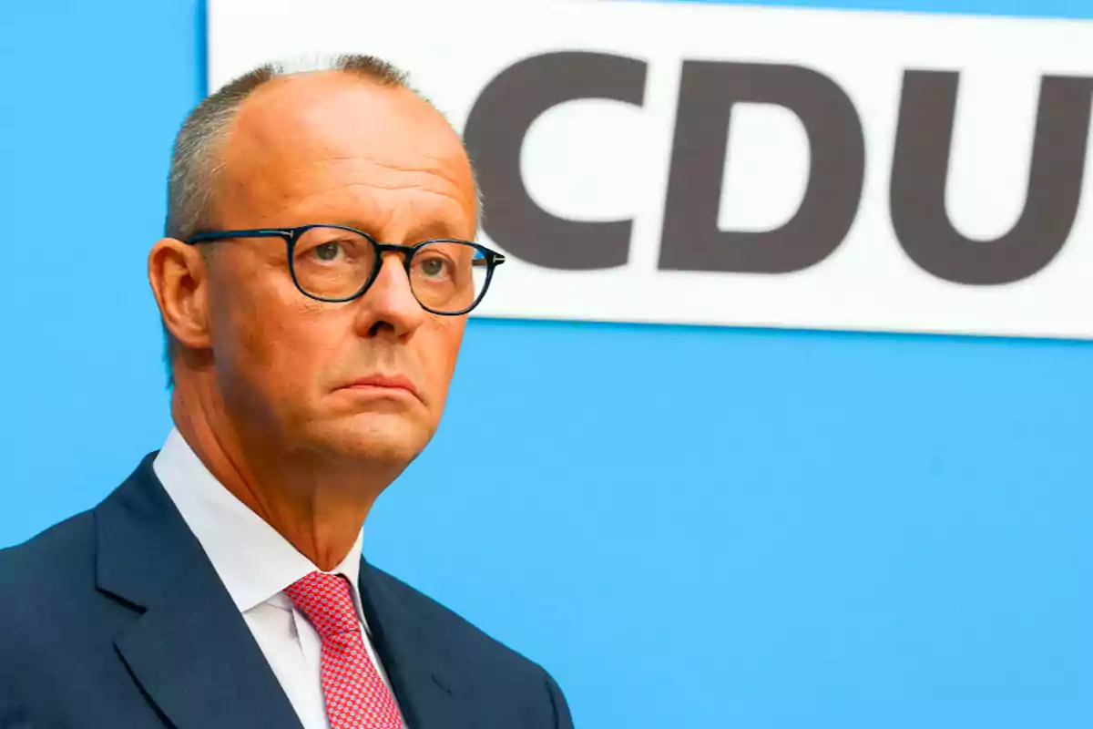 Man with glasses and suit in front of a blue background with the CDU logo.