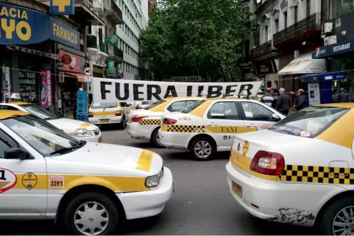 A group of taxis blocks a street in a protest, with a large sign that says 