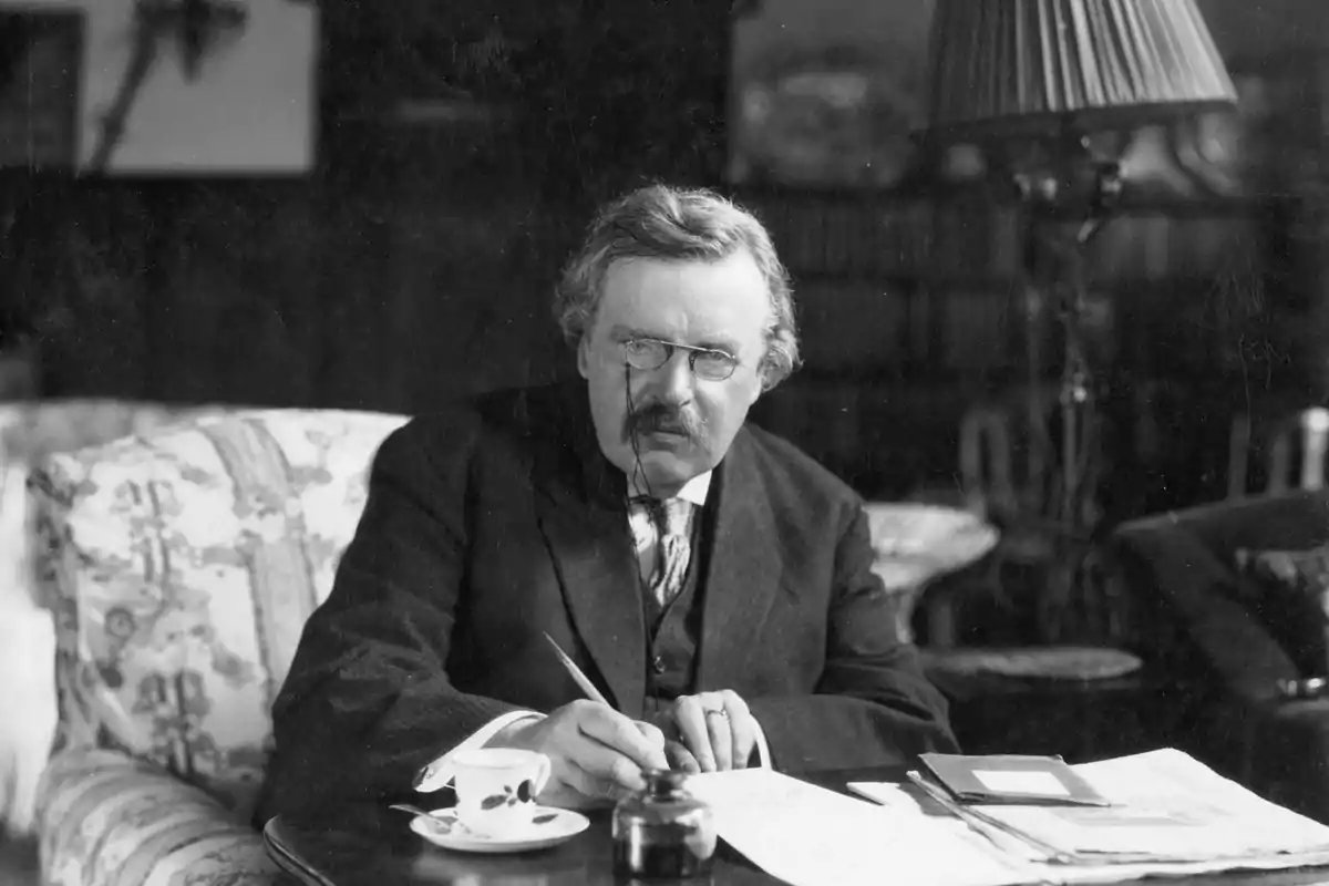 Hombre de bigote y gafas escribiendo en un escritorio con papeles y una taza de té Hombre de bigote y gafas escribiendo en un escritorio con papeles y una taza de té