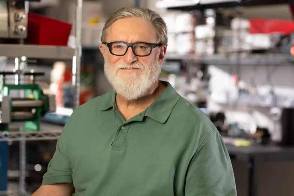 Older man with a beard and glasses smiles while standing in a laboratory or workshop setting, wearing a green polo jersey. Older man with a beard and glasses smiles while standing in a laboratory or workshop setting, wearing a green polo jersey.