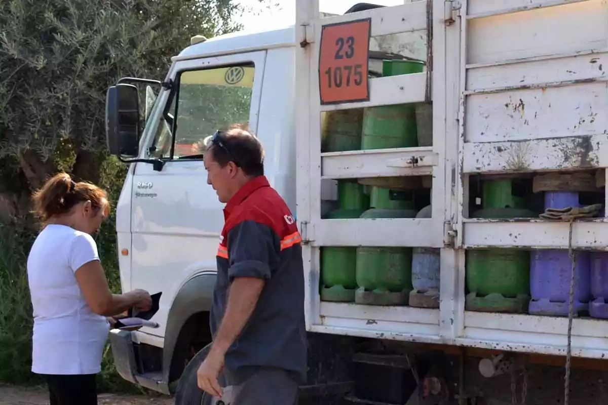 Una mujer y un hombre junto a un camión de reparto de garrafas de gas, el hombre viste uniforme de trabajo y la mujer revisa su cartera Una mujer y un hombre junto a un camión de reparto de garrafas de gas, el hombre viste uniforme de trabajo y la mujer revisa su cartera