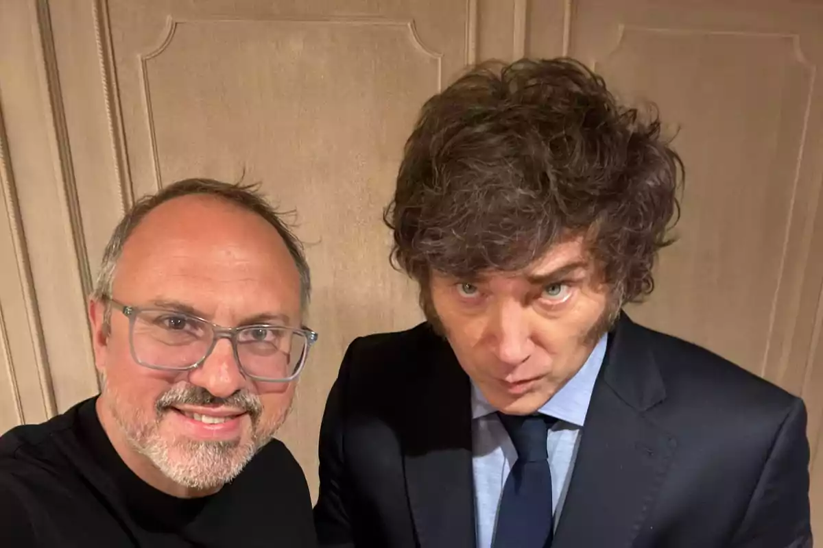 Dos hombres posan para una selfie en un ambiente interior, uno de ellos lleva gafas y el otro viste traje y corbata. Dos hombres posan para una selfie en un ambiente interior, uno de ellos lleva gafas y el otro viste traje y corbata.
