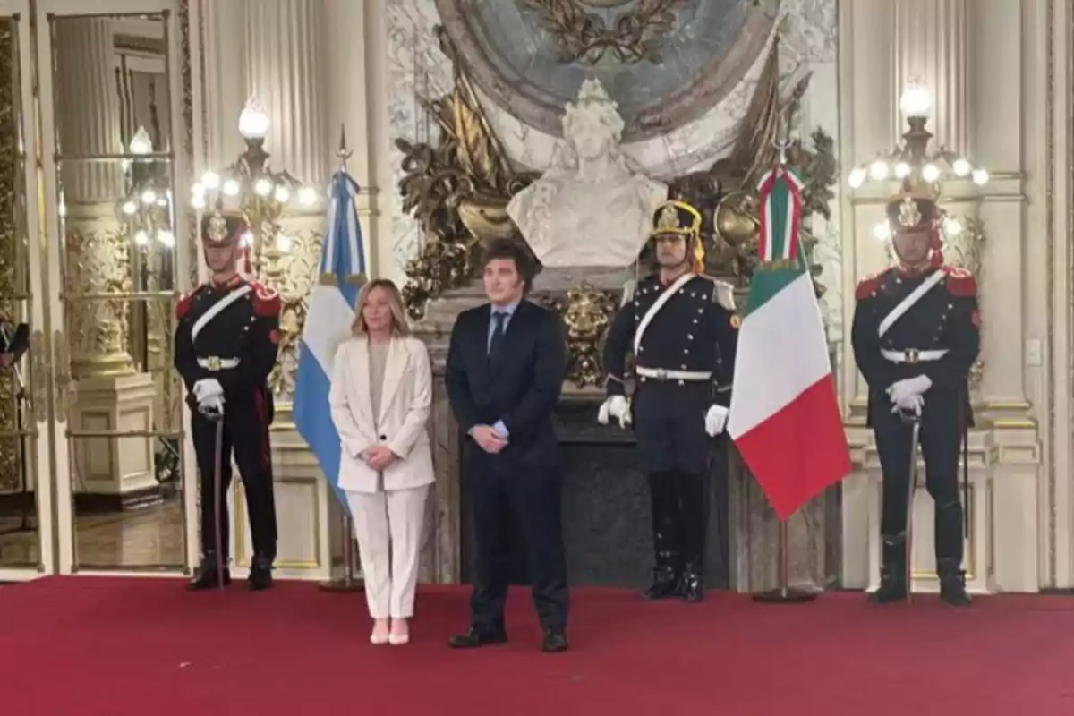 Personas posando en un salón elegante con banderas de Argentina e Italia y guardias uniformados.