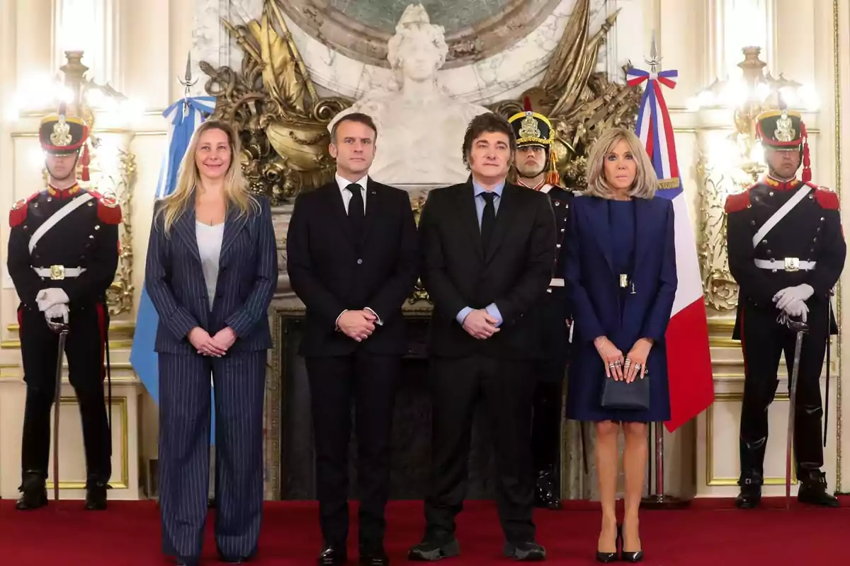 Un grupo de personas posando en un salón elegante con guardias uniformados y banderas de fondo.