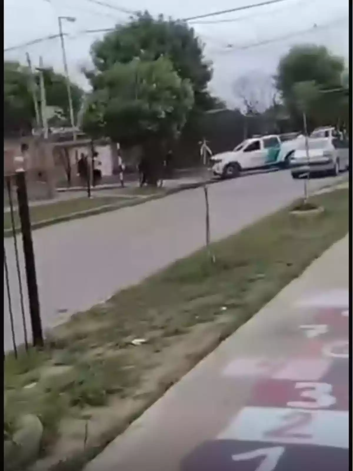 Una calle tranquila con un árbol grande y una camioneta blanca estacionada cerca de la acera, mientras en el suelo hay un juego de rayuela pintado.