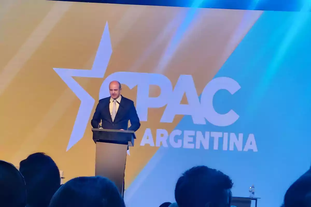 Un hombre de traje hablando en un podio con el logo de CPAC Argentina de fondo.