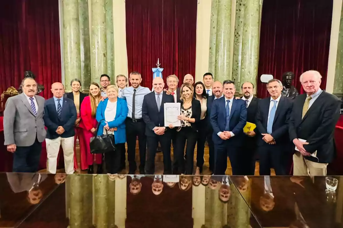 Un grupo de personas posando juntas en un salón con cortinas rojas y columnas verdes.