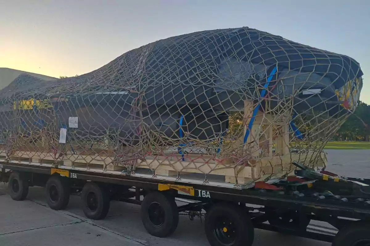 Un objeto grande cubierto con una red de carga sobre un remolque en un área al aire libre.