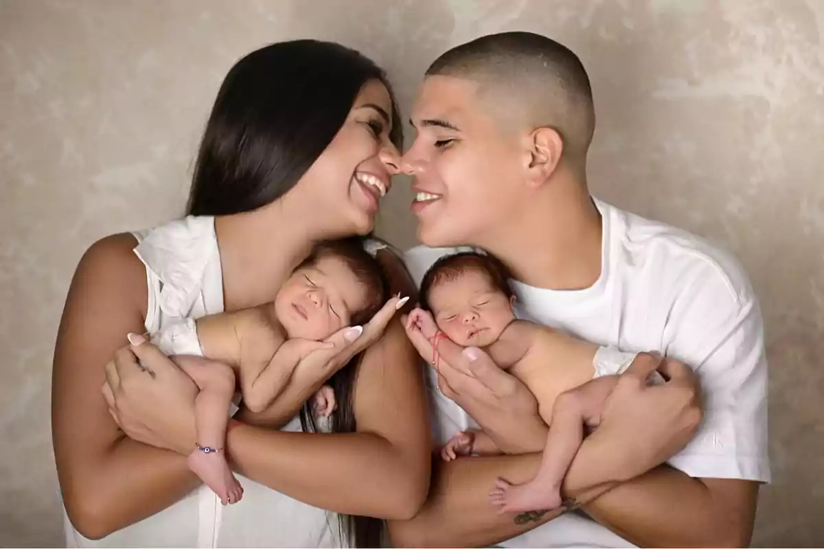 A smiling couple holds two newborn babies in their arms. A smiling couple holds two newborn babies in their arms.