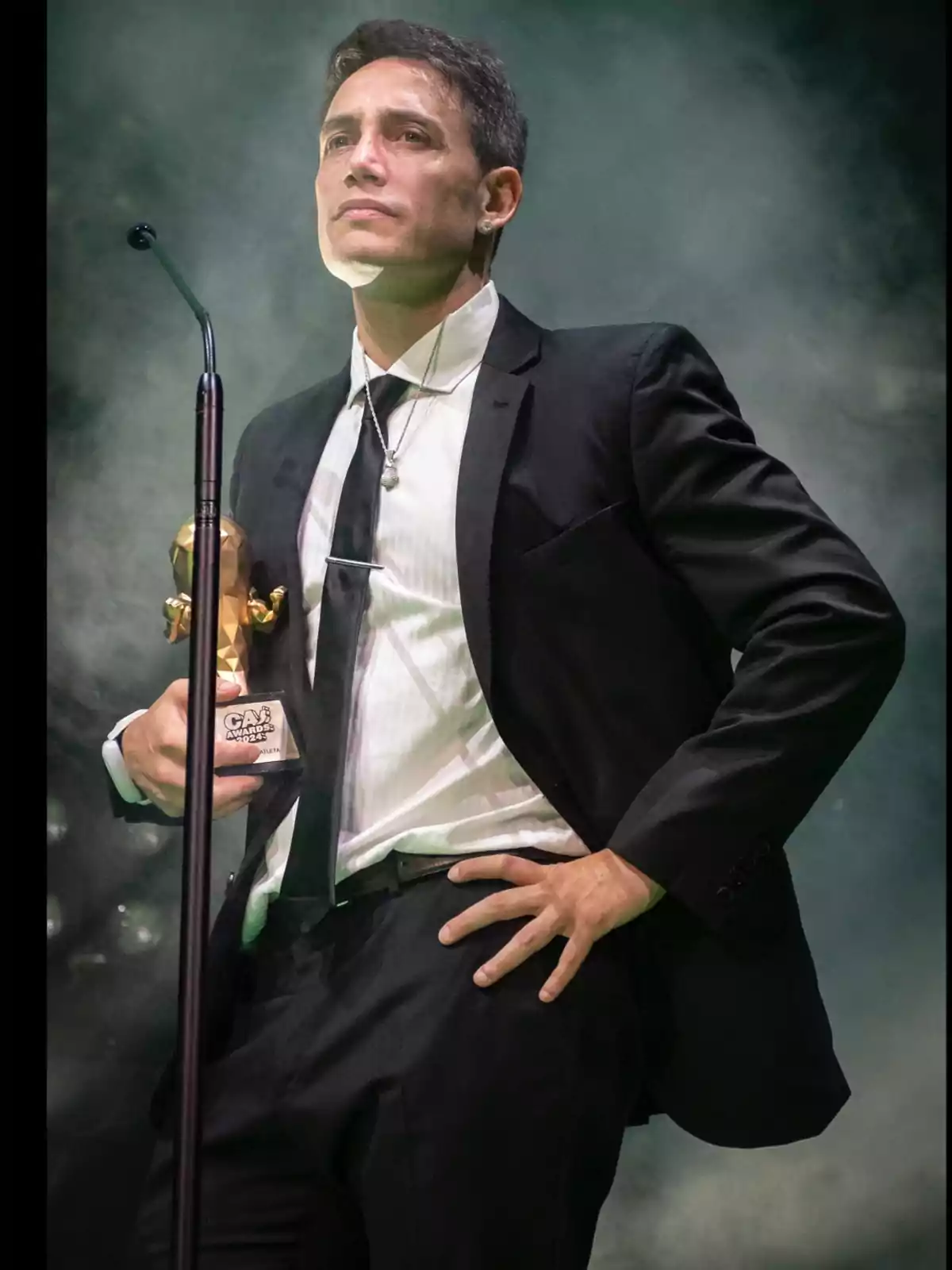 Hombre de traje sosteniendo un trofeo en el escenario con fondo de humo Hombre de traje sosteniendo un trofeo en el escenario con fondo de humo