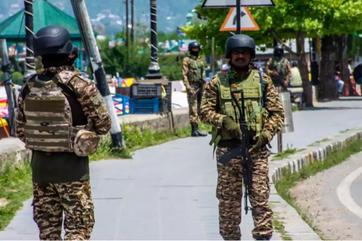 Soldiers in camouflage uniforms and helmets patrol a street with trees and traffic signs. Soldiers in camouflage uniforms and helmets patrol a street with trees and traffic signs.