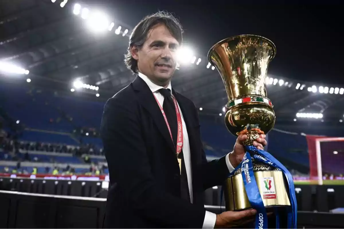 Man in a suit holding a golden trophy in a lit stadium Man in a suit holding a golden trophy in a lit stadium