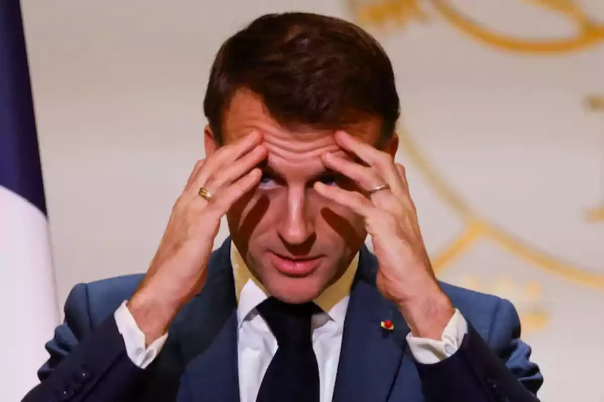 Man in a blue suit and black tie puts his hands to his forehead with a worried expression