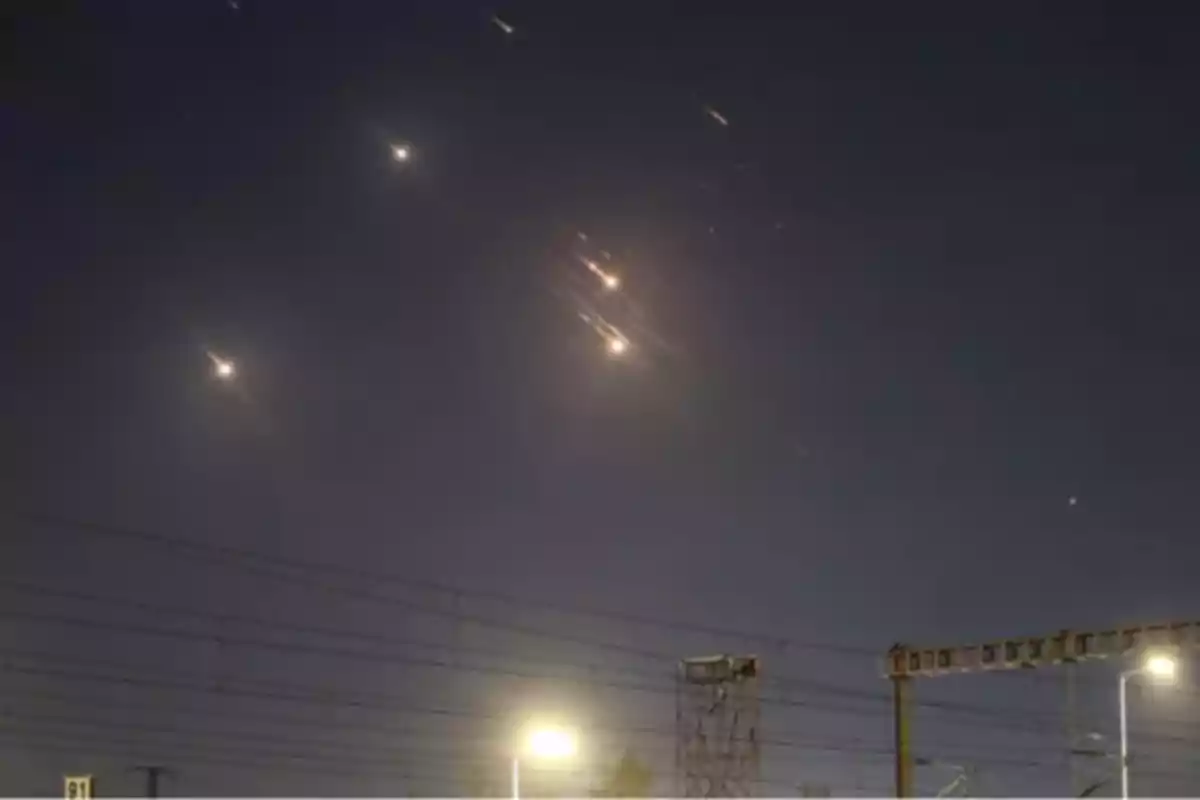 Varios destellos luminosos cruzan el cielo nocturno sobre una zona urbana con cables eléctricos y postes visibles en primer plano Varios destellos luminosos cruzan el cielo nocturno sobre una zona urbana con cables eléctricos y postes visibles en primer plano