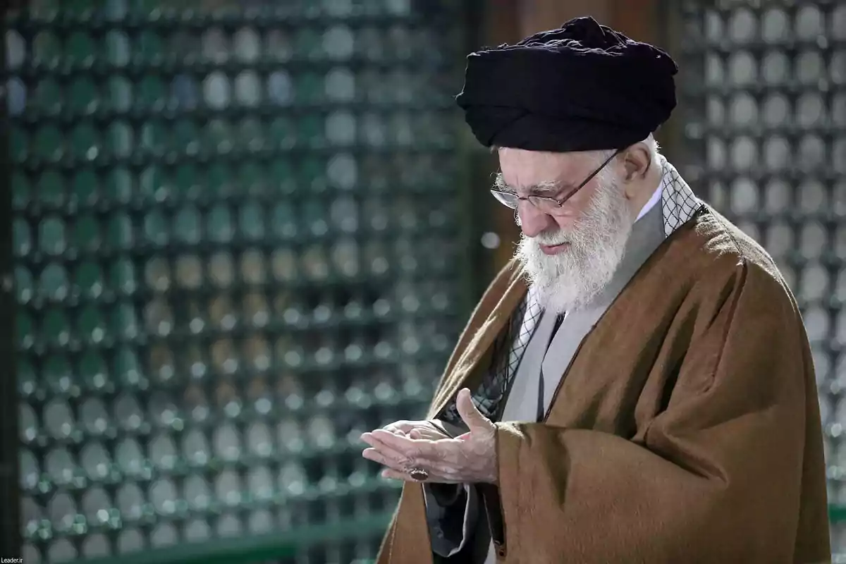 Elderly man with a white beard and a black turban praying with his hands raised in a place with a green lattice background Elderly man with a white beard and a black turban praying with his hands raised in a place with a green lattice background