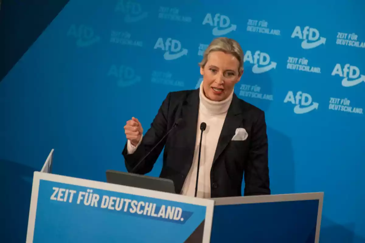 Una persona hablando en un podio con un fondo azul que tiene el logotipo de AfD y el texto Una persona hablando en un podio con un fondo azul que tiene el logotipo de AfD y el texto