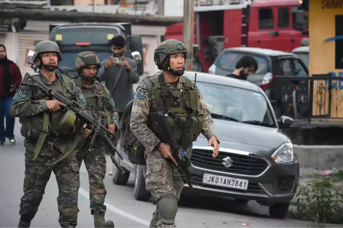 Soldados armados caminan por una calle urbana mientras personas observan y toman fotos.