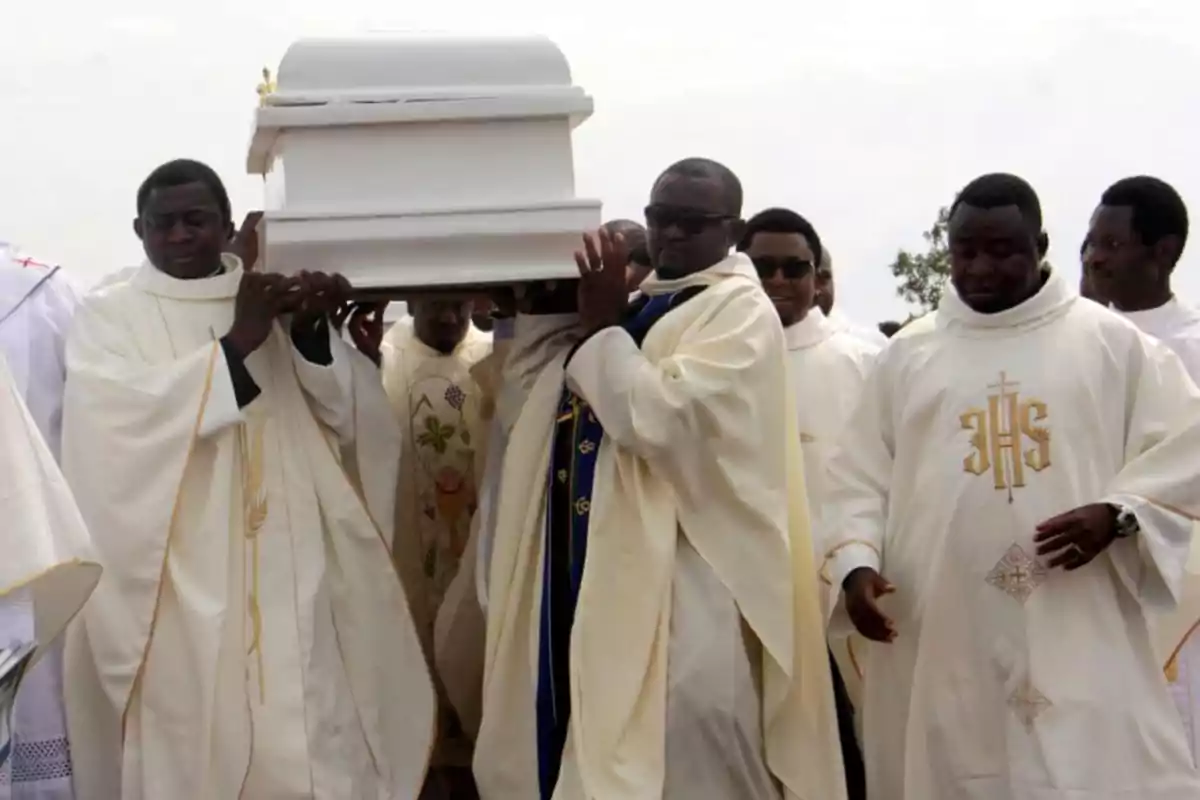 A group of priests dressed in white robes carries a white coffin during a funeral procession. A group of priests dressed in white robes carries a white coffin during a funeral procession.