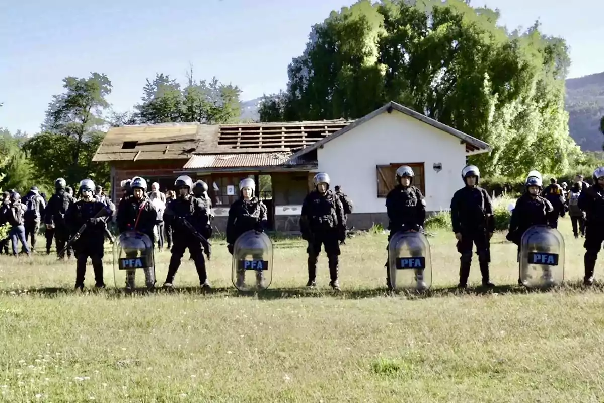 Un grupo de policías con equipo antidisturbios se encuentra frente a una casa en un área rural. Un grupo de policías con equipo antidisturbios se encuentra frente a una casa en un área rural.
