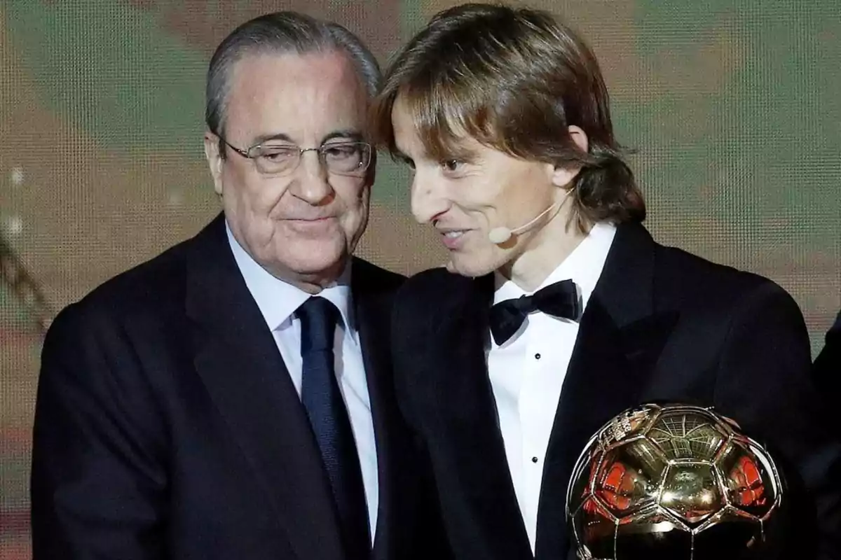 Two men in formal suits, one of them holding a golden trophy. Two men in formal suits, one of them holding a golden trophy.