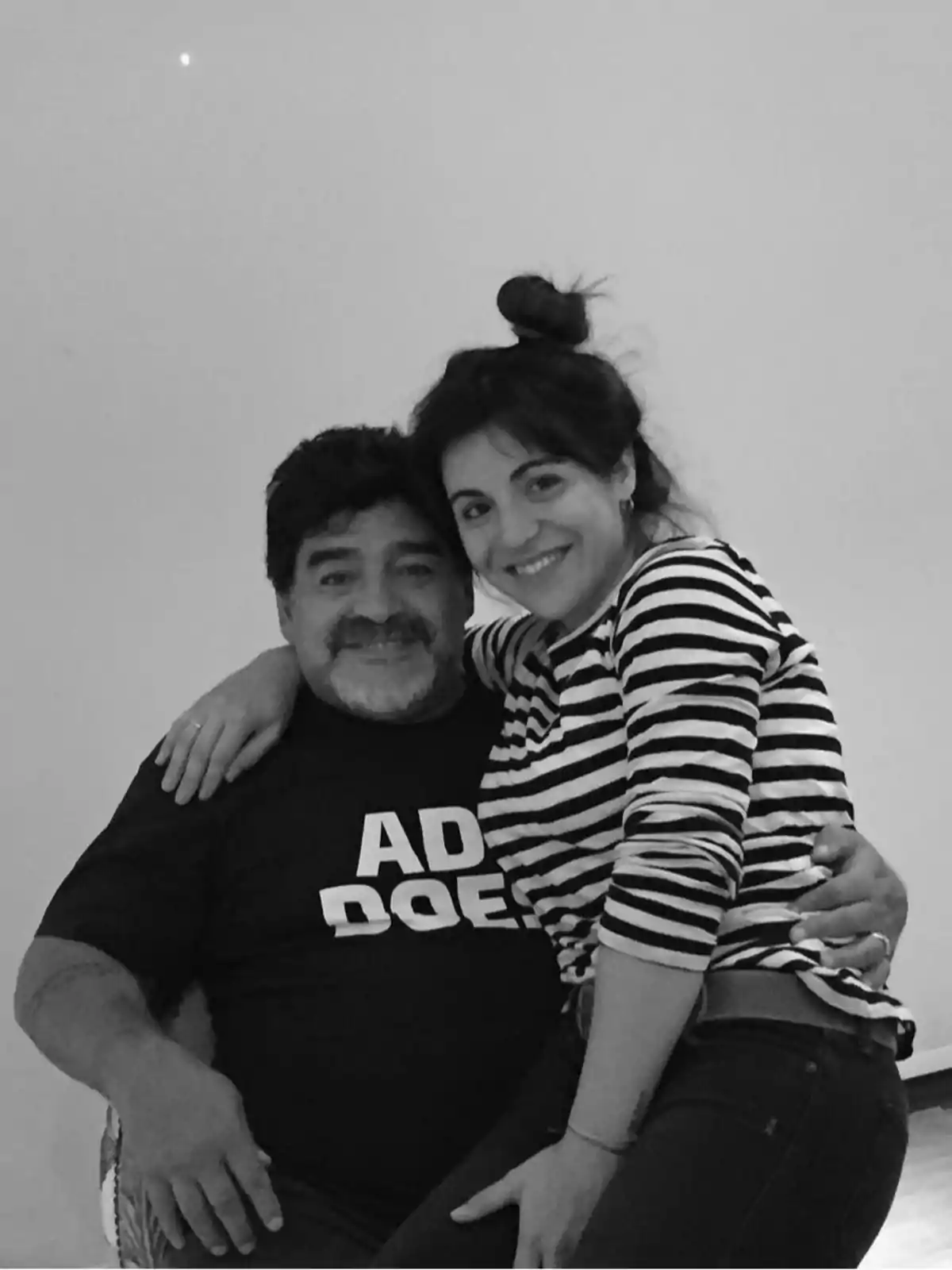 Un hombre y una mujer sonríen mientras posan juntos, la mujer está sentada sobre las piernas del hombre y ambos se ven felices en una foto en blanco y negro Un hombre y una mujer sonríen mientras posan juntos, la mujer está sentada sobre las piernas del hombre y ambos se ven felices en una foto en blanco y negro
