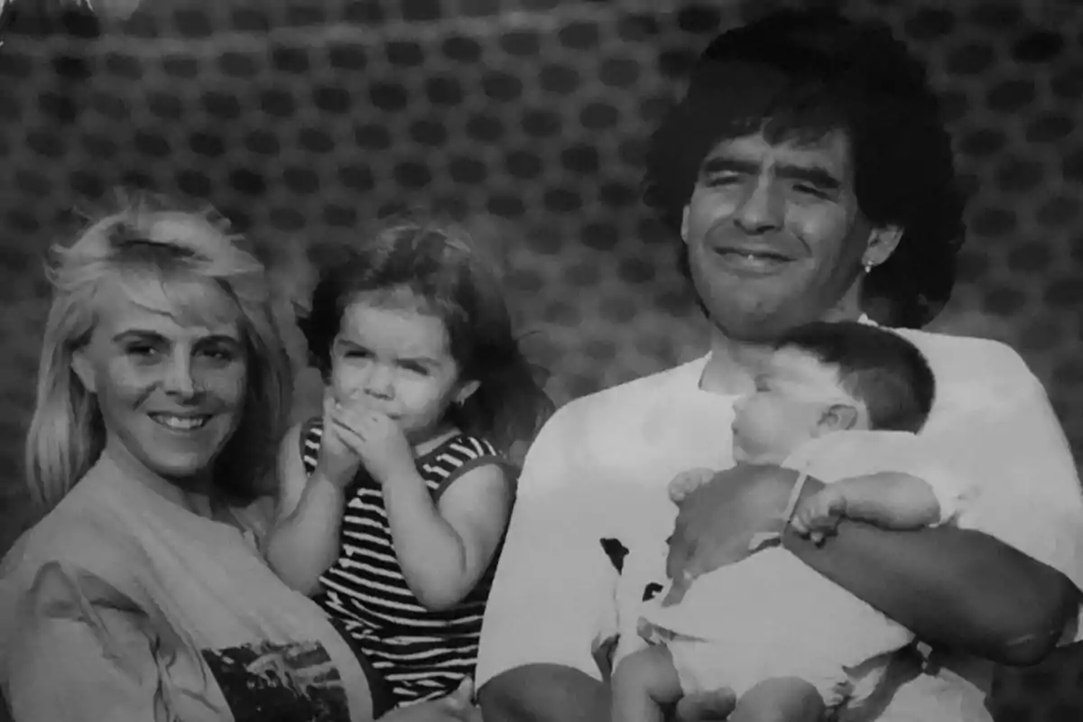 Una familia sonriente posa para una foto en blanco y negro, con una mujer sosteniendo a una niña pequeña y un hombre sosteniendo a un bebé. Una familia sonriente posa para una foto en blanco y negro, con una mujer sosteniendo a una niña pequeña y un hombre sosteniendo a un bebé.