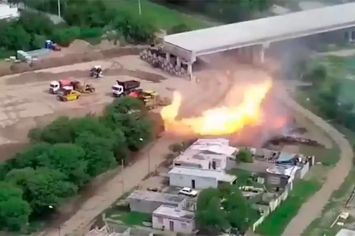 Vista aérea de un incendio en una zona industrial con vehículos de construcción y edificios cercanos.