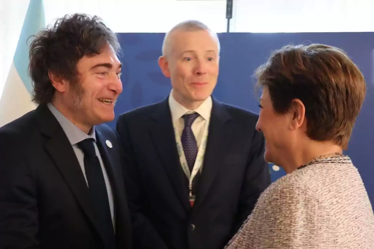 Tres personas vestidas de traje conversan y sonríen en un evento formal.