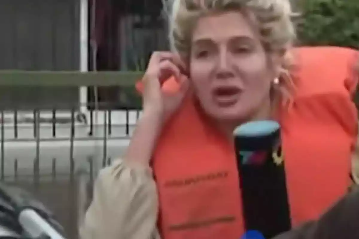 Una persona con chaleco salvavidas naranja hablando frente a un micrófono. Una persona con chaleco salvavidas naranja hablando frente a un micrófono.