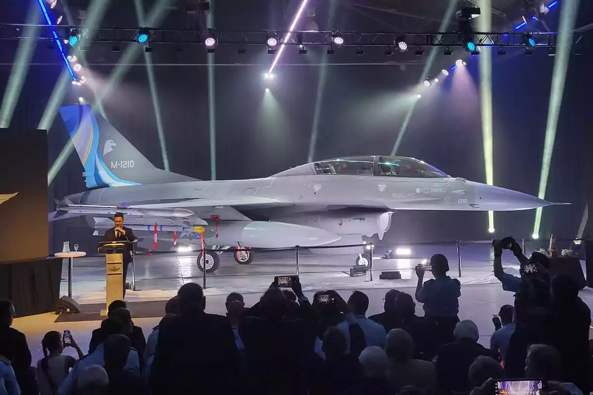 Un avión de combate en exhibición en un evento con luces brillantes y una audiencia observando.