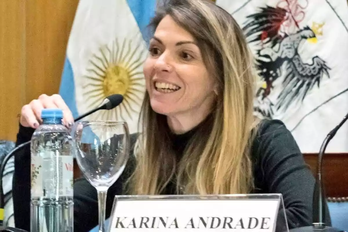 Una persona hablando en un micrófono con una bandera de Argentina de fondo.