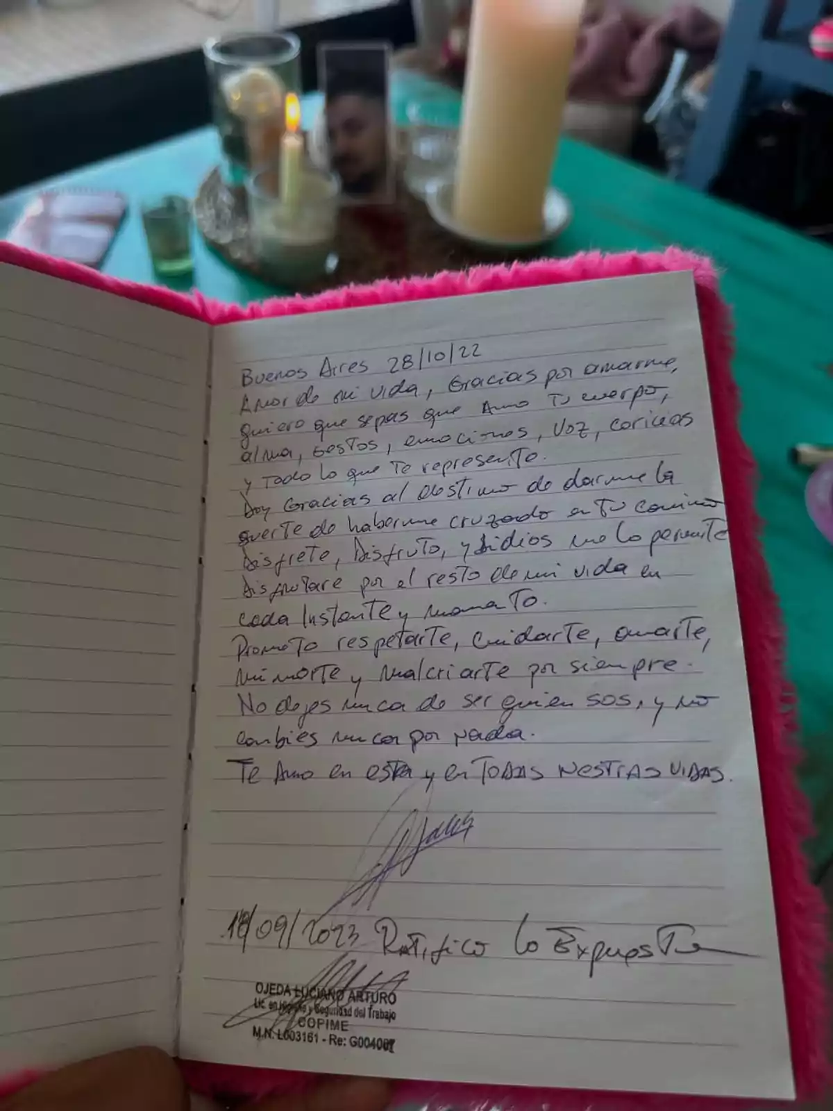 A notebook with a handwritten love letter, on a table with lit candles, a photo, and personal items in the background. A notebook with a handwritten love letter, on a table with lit candles, a photo, and personal items in the background.